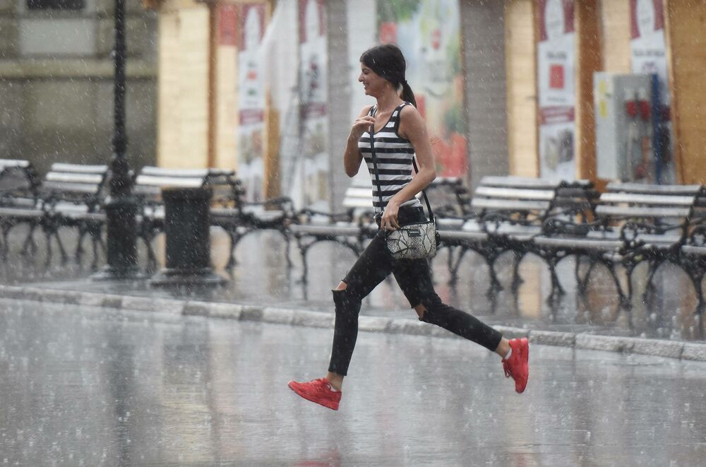 Devojka koja pretrčava ulicu dok pljušti kiša 