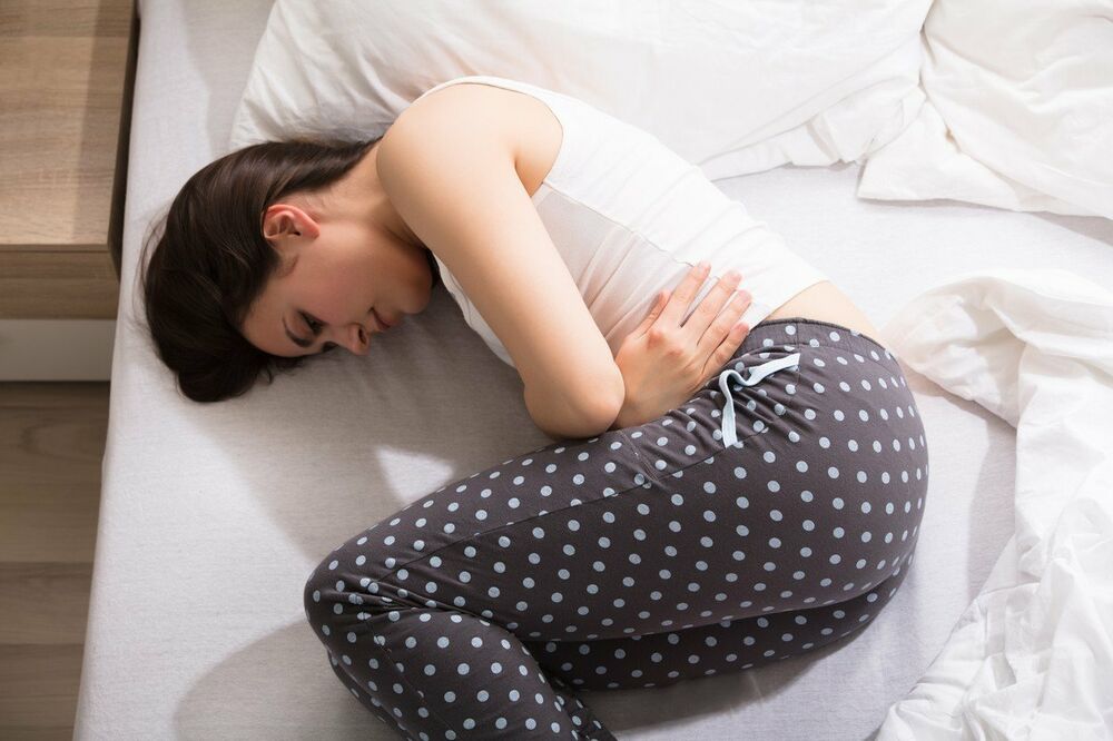 Žena sa bolom u stomaku leži na krevetu